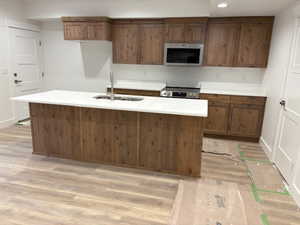Kitchen featuring stainless steel appliances, wood finish cabinetry, light wood-style floors, and a center island with sink