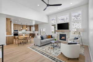 Enhanced staged photo. Living area with light wood-style flooring, a high ceiling, a tile fireplace, ceiling fan, and recessed lighting