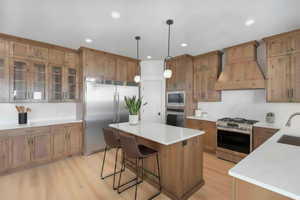 Kitchen featuring a breakfast bar, built in appliances, wood finish cabinets, decorative light fixtures, and light wood-type flooring