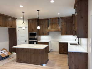 Kitchen with light stone countertops, stainless steel appliances, a center island, hanging light fixtures, and light wood-style flooring