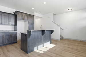Kitchen with light stone countertops, light wood-style flooring, a kitchen bar, a center island, and dark wood finish cabinets