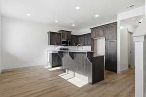 Kitchen featuring a breakfast bar, an island with sink, dark wood finish cabinetry, light wood-style flooring, and recessed lighting