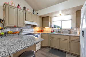 Kitchen with white appliances, light stone counters, light wood-style flooring, a breakfast bar area, and decorative backsplash