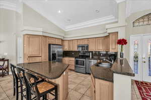 Kitchen featuring a kitchen bar, vaulted ceiling, stainless steel appliances, tasteful backsplash, and dark stone counters