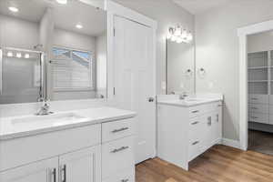 Bathroom featuring two vanities, light wood-type flooring, a shower stall, and a walk in closet