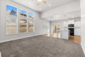 Kitchen with open floor plan, white cabinets, a kitchen island with sink, a ceiling fan, and black appliances