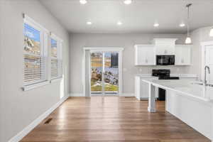 Kitchen with white cabinetry, black appliances, decorative light fixtures, light wood-type flooring, and light stone countertops