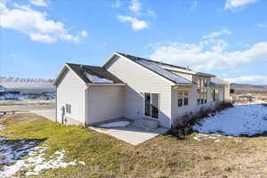 Snow covered property featuring a mountain view, a patio, a lawn, and entry steps