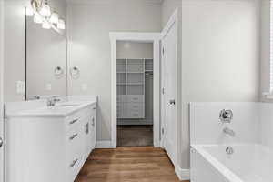 Full bath featuring vanity, a garden tub, light wood finished floors, and a spacious closet