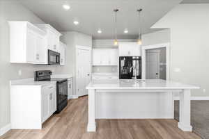 Kitchen with black appliances, white cabinets, decorative light fixtures, a kitchen island with sink, and a kitchen bar