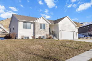 View of front facade with board and batten siding, a front lawn, a garage, stone siding, and a shingled roof