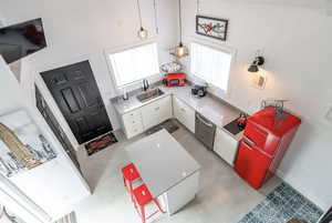Kitchen featuring white cabinets, light countertops, a high ceiling, stainless steel dishwasher, and fridge