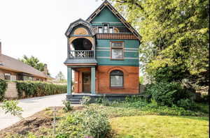 Victorian home with a balcony, a front lawn, and concrete driveway