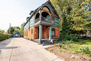 Victorian house with a porch, an outbuilding, driveway, a balcony, and brick siding