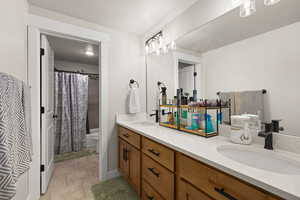 Bathroom featuring double vanity, shower / bath combo, a textured ceiling, and light tile patterned floors