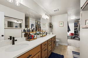 Bathroom with a spacious closet, double vanity, a textured ceiling, and light tile patterned floors