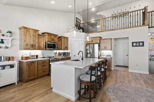 Dual tone kitchen featuring decorative light fixtures, decorative backsplash, a kitchen breakfast bar, a center island with sink, and light wood finished floors
