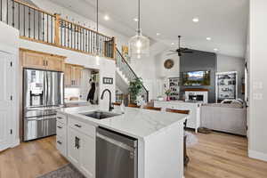 Kitchen with stainless steel appliances, hanging light fixtures, light wood finished floors, vaulted ceiling, and open floor plan