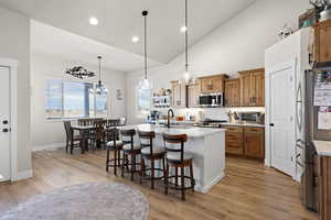 Two tone kitchen with decorative light fixtures, stainless steel appliances, light wood-style flooring, lofted ceiling, and a kitchen bar