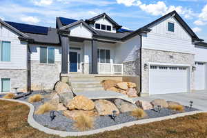View of front facade with stone siding, covered porch, board and batten siding, solar panels, and driveway