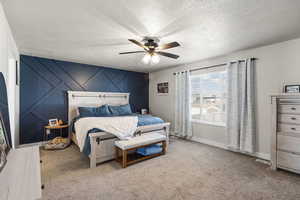 Carpeted bedroom featuring an accent wall, ceiling fan, and a textured ceiling