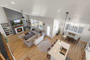 Living room with light wood-type flooring, a warm lit fireplace, a ceiling fan, and a high textured ceiling