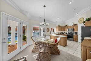 Dining area with lofted ceiling, hanging lights, ornamental molding, light colored carpet, and light tile patterned floors