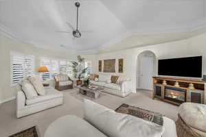Carpeted living area featuring arched walkways, ceiling fan, lofted ceiling, and ornamental molding