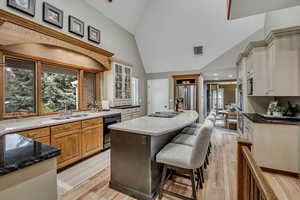 Dual tone kitchen with dark stone counters, vaulted ceiling, a kitchen bar, stainless steel appliances, and light wood finished floors