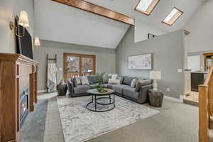 Living room featuring light carpet, lofted ceiling, a fireplace, and a skylight