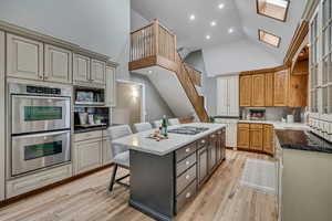 Two tone kitchen featuring a kitchen breakfast bar, stainless steel appliances, a kitchen island, light stone counters, and two tone color scheme
