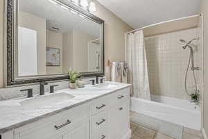 Bathroom with double vanity, shower / bath combo with shower curtain, a textured ceiling, and light tile patterned floors