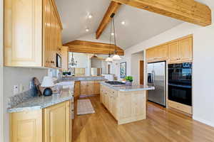 Kitchen with light wood finish cabinets, hanging light fixtures, stainless steel appliances, beam ceiling, and a kitchen island