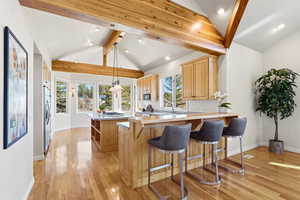 Kitchen featuring a peninsula, a center island, light wood finish cabinetry, a breakfast bar, and beam ceiling