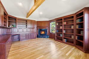 Unfurnished office featuring lofted ceiling with beams, built in desk, light wood finished floors, a high end fireplace, and built in features