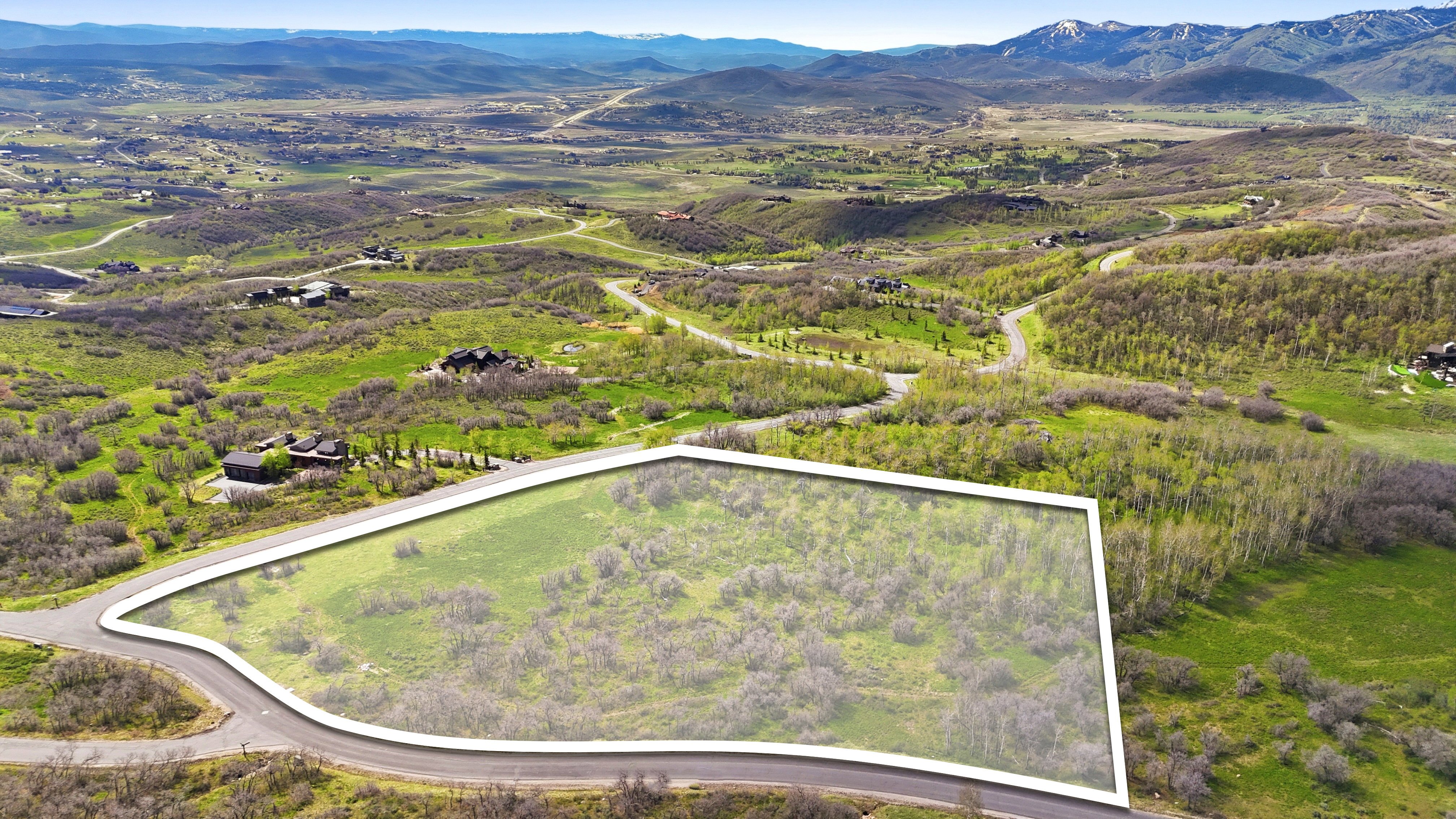 Expansive parcel of undeveloped land outlined by a paved road, featuring natural foliage and a mountainous backdrop