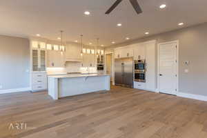 Kitchen with white cabinetry, glass fronted cabinets, stainless steel appliances, a ceiling fan, and a breakfast bar area