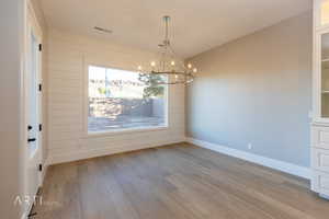 Unfurnished dining area featuring wood-type flooring, wooden walls, and a chandelier