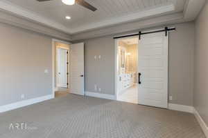 Unfurnished bedroom with a barn door, light colored carpet, wooden ceiling, ensuite bathroom, and ceiling fan