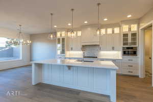 Kitchen featuring white cabinets, glass fronted cabinets, light stone counters, decorative backsplash, and dark wood-style floors