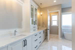 Bathroom with double vanity, a freestanding tub, light marble finish floors, and recessed lighting