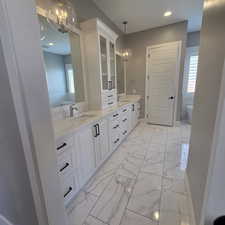 Full bathroom featuring hanging lights, double vanity, light marble finish floors, and a soaking tub