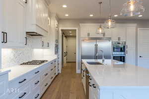 Kitchen featuring light stone counters, white cabinets, pendant lighting, dark wood-style floors, and stainless steel appliances