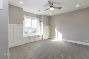 Spare room with a ceiling fan, a decorative wall, light carpet, wainscoting, and recessed lighting
