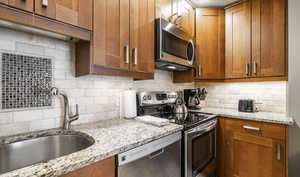 Kitchen featuring stainless steel appliances, light stone countertops, backsplash, and wood finish cabinetry