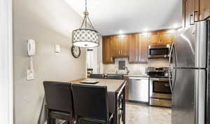 Kitchen with stainless steel appliances, hanging light fixtures, wood finish cabinets, a textured wall, and backsplash