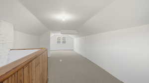 Hallway with lofted ceiling and light colored carpet