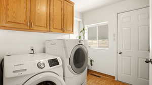 Laundry room featuring washing machine and clothes dryer, cabinet space, and parquet floors