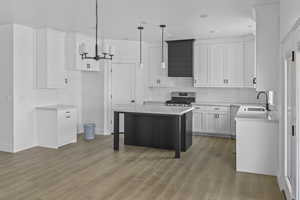 Kitchen with hanging light fixtures, a center island, a breakfast bar, gas range, and light wood-style floors