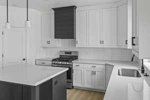 Dual tone kitchen featuring stainless steel range with gas cooktop, backsplash, light wood finished floors, pendant lighting, and two tone cabinets